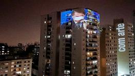 The government of Jair Bolsonaro has been severely criticized for its flawed handling of the COVID-19 pandemic. Here, an image of Bolsonaro failing to put on a mask properly is screened on a building as a mark of protest. Photo: Brasil De Fato