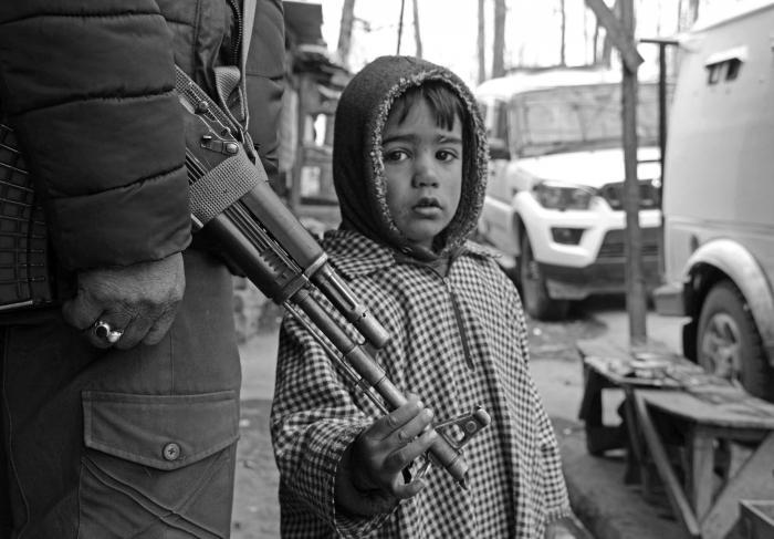 (Picture: A boy, after being removed from an encounter site, holds the gun of a policeman in Tral village of Pulwama where a gunfight between militants and government forces was underway on June 25, 2020.) Picture: Kamran Yousuf/NewsClick