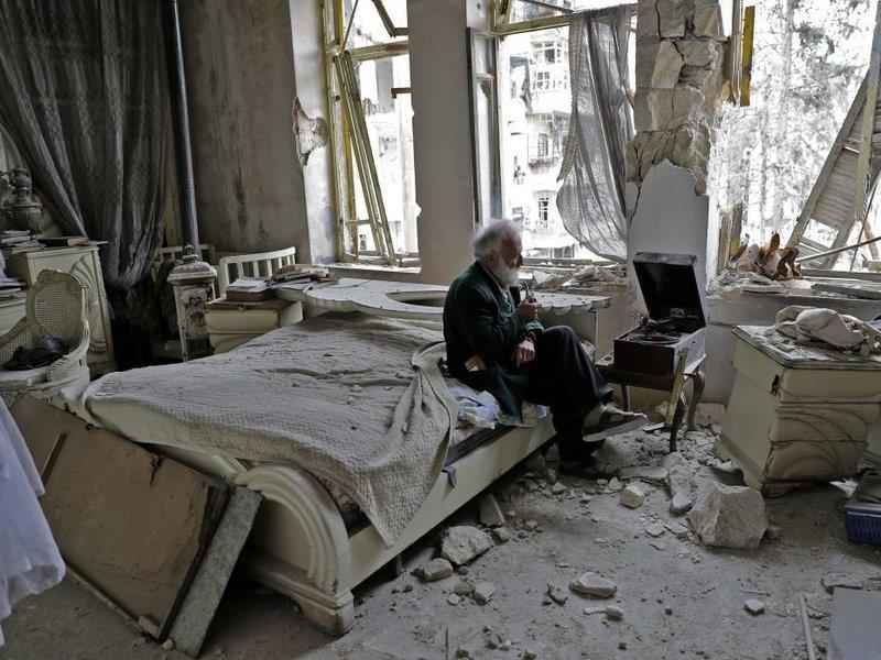 Abu Omar, 70, smokes his pipe as he sits in his destroyed bedroom listening to music on his gramophone in the neighbourhood of al-Shaar in Aleppo, Syria.