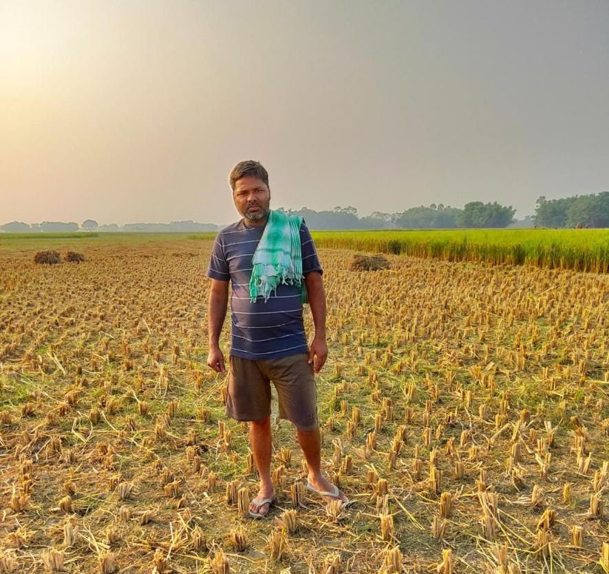 Trilok Das standing in his field And near a stored corn