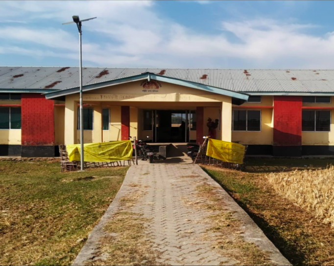 The Bihmari and Bongaon PHC situated amidst a rice field, with a narrow path leading to the building.