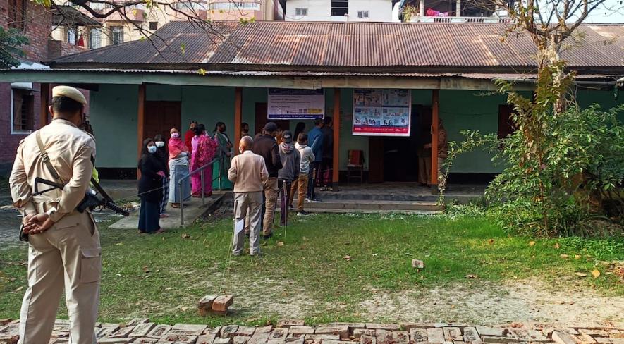 Police personnel stand guard while voters wait in a queue to cast their votes for the first phase of Manipur Assembly elections, at a polling booth, in Kangpokpi on Monday.