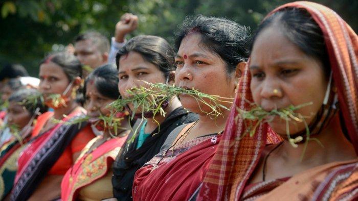 'Gaon Sathi' women workers put grass in their mouth as they stage a protest demanding hike in their monthly wages and to give them permanent status.