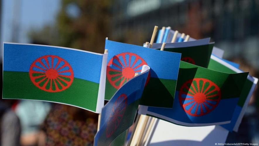 The Roma flag is dark blue and green, representing the heavens and earth, with a chakra wheel in the center in recognition of Indian heritage.